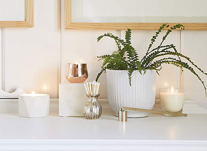 Prateleira decorada com velas aromáticas acesas, difusor de aromas, vaso com samambaia e acessórios em ambiente claro e elegante.