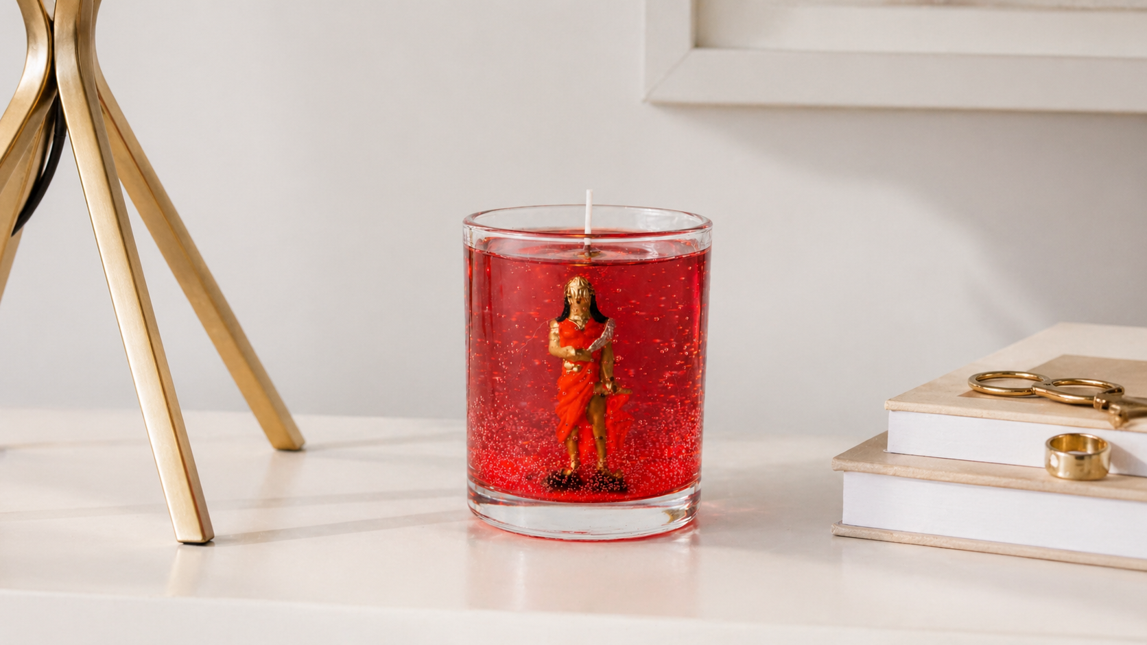 Vela em gel vermelha com imagem de Iansã em recipiente de vidro transparente sobre mesa decorativa.
