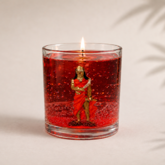 Vela em Gel Iansã artesanal em copo de vidro redondo com parafina em gel vermelha translúcida, contendo uma representação de Iansã em seu interior. A vela está acesa e posicionada sobre fundo claro com iluminação suave e sombras delicadas de folhagens.