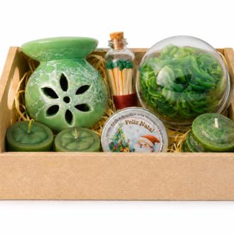 Kit Aromático Decorativo composto por aromatizador cerâmico verde com acabamento marmorizado, vela artesanal floral em formato de rosa protegida por redoma transparente, fósforos decorativos em frasco de vidro, mini velas aromáticas e lata temática natalina. Os itens estão organizados em uma elegante bandeja decorativa com enchimento de palha sobre fundo branco, destacando os detalhes artesanais e a sofisticação do conjunto.