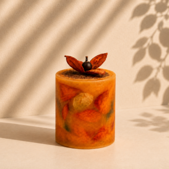 Vela Aromática Botânica artesanal em formato cilíndrico, confeccionada com cera translúcida em tons quentes de âmbar, laranja e dourado, incorporando folhas naturais preservadas em sua composição. O topo é decorado com delicadas folhas secas em formato floral, criando uma peça sofisticada, acolhedora e inspirada na beleza dos elementos naturais.