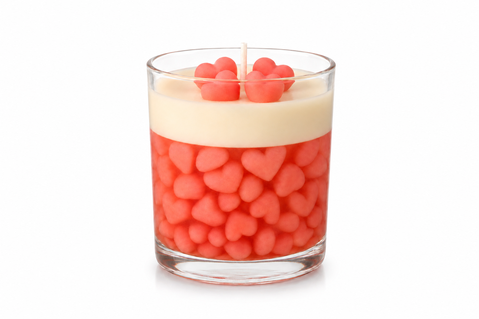 Vela aromática decorativa em recipiente de vidro transparente preenchido com delicados corações rosas, finalizada com camada cremosa de cera e detalhes em formato de coração na superfície.