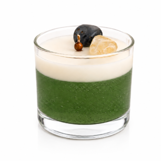 Vela Aromática de Cristais em copo de vidro transparente, composta por uma camada inferior verde translúcida e uma camada superior cremosa. A decoração inclui cristais naturais e elementos ornamentais delicados posicionados sobre a superfície da vela. A imagem apresenta fundo branco, iluminação suave e estilo clean, destacando os detalhes artesanais da peça.