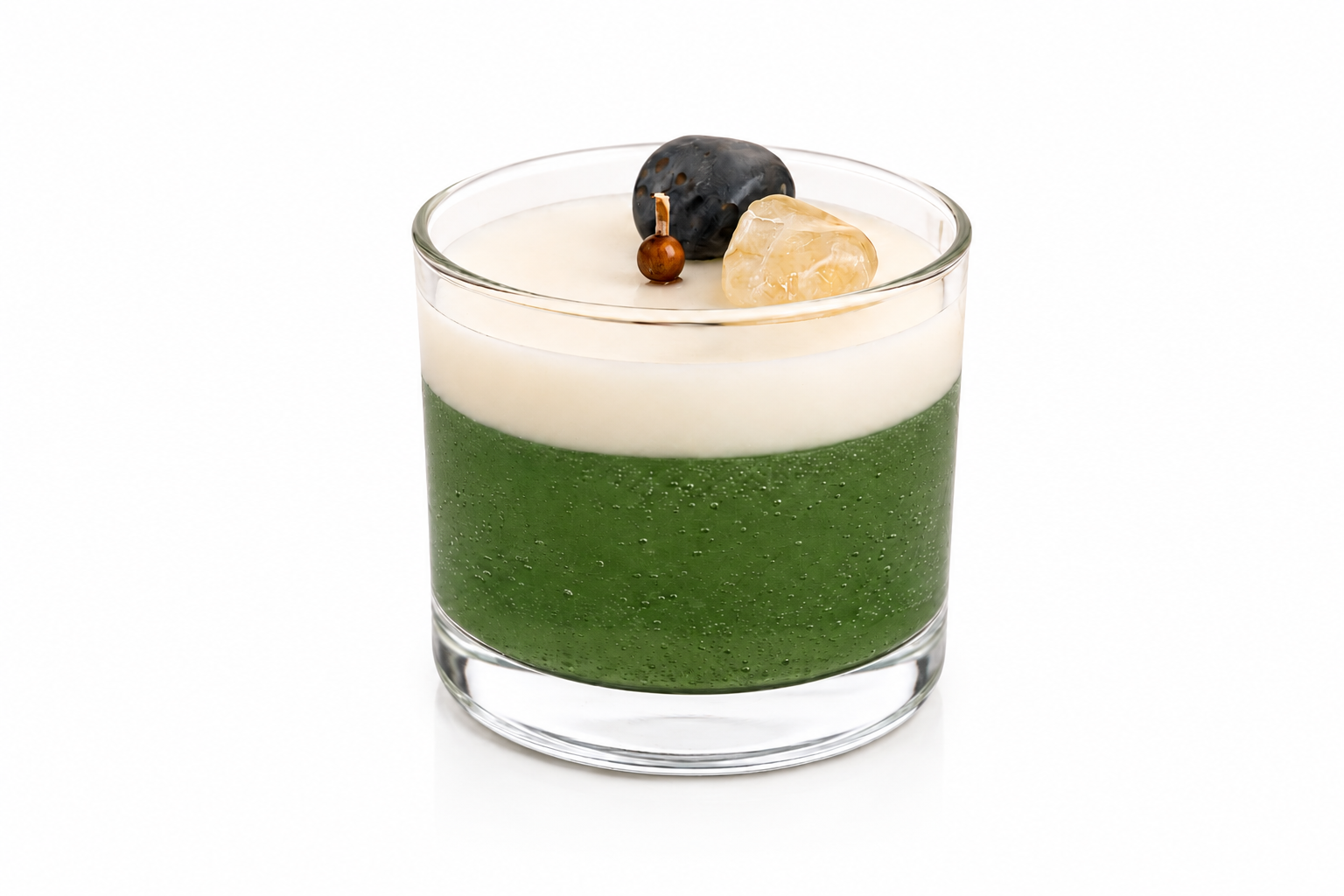 Vela Aromática de Cristais em copo de vidro transparente, composta por uma camada inferior verde translúcida e uma camada superior cremosa. A decoração inclui cristais naturais e elementos ornamentais delicados posicionados sobre a superfície da vela. A imagem apresenta fundo branco, iluminação suave e estilo clean, destacando os detalhes artesanais da peça.