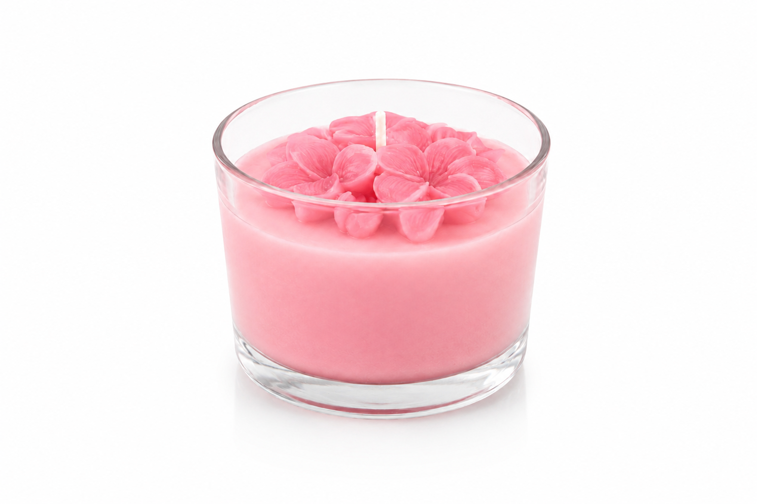 Vela Aromática de Flor de Jasmim em copo de vidro transparente, com cera rosa delicada e flores ornamentais inspiradas no jasmim moldadas na superfície, fotografada em fundo branco de estúdio que destaca seu design artesanal e acabamento sofisticado.