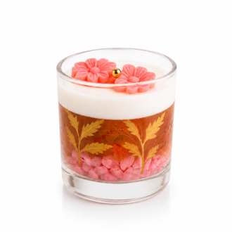 Vela Aromática Floral Rosé artesanal em copo de vidro transparente, com camada superior de parafina branca, flores decorativas rosadas, gel translúcido em tom rosé com folhas douradas ornamentais e pedras decorativas rosadas, apresentada em fundo branco para catálogo de produtos.