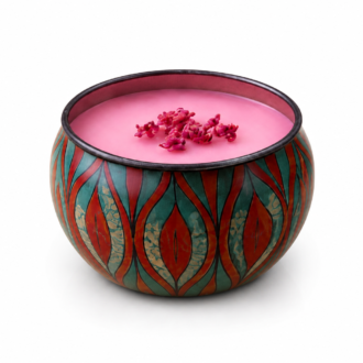 Vela aromática em lata decorativa com estampa artística em tons de vermelho e verde, preenchida com cera rosa e delicados elementos florais sobre a superfície, apresentada em fundo branco.