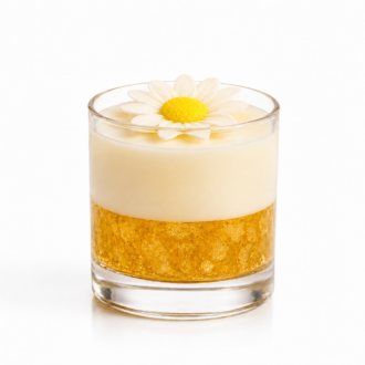 Vela Aromática Margarida artesanal em copo de vidro transparente, composta por uma camada inferior dourada com cristais decorativos e uma camada superior em tom creme suave. No topo, uma delicada margarida branca com centro amarelo complementa o design elegante da peça. A vela está fotografada sobre fundo branco, destacando seus detalhes, transparência do vidro e acabamento sofisticado.