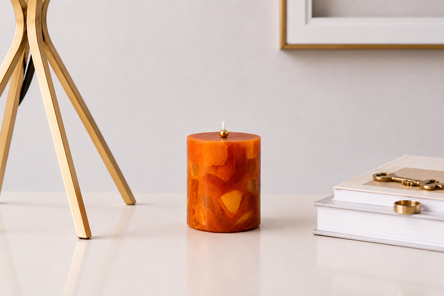 Vela aromática mosaico em tons âmbar e dourado posicionada sobre uma mesa clara, acompanhada por livros decorativos e detalhes dourados, em uma composição elegante e minimalista.