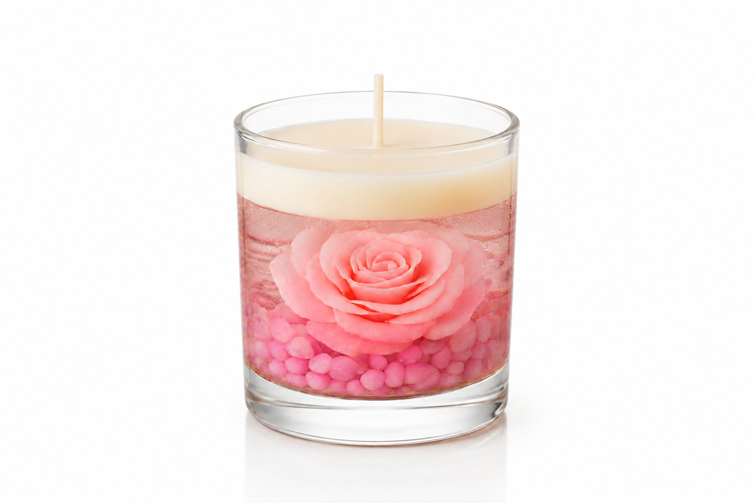 Vela Aromática Rosa Imersa em copo de vidro transparente, contendo uma rosa rosa preservada no interior de parafina em gel cristalina sobre pequenas pedras decorativas rosadas. A peça possui camada superior de cera branca e está apresentada em fundo branco, destacando seus detalhes artesanais e acabamento sofisticado.