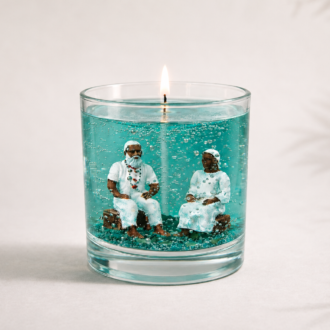Vela em gel azul-turquesa com miniaturas artesanais de um casal de Pretos Velhos em seu interior, acesa sobre fundo claro minimalista com sombras suaves, destacando a transparência e os detalhes da composição.
