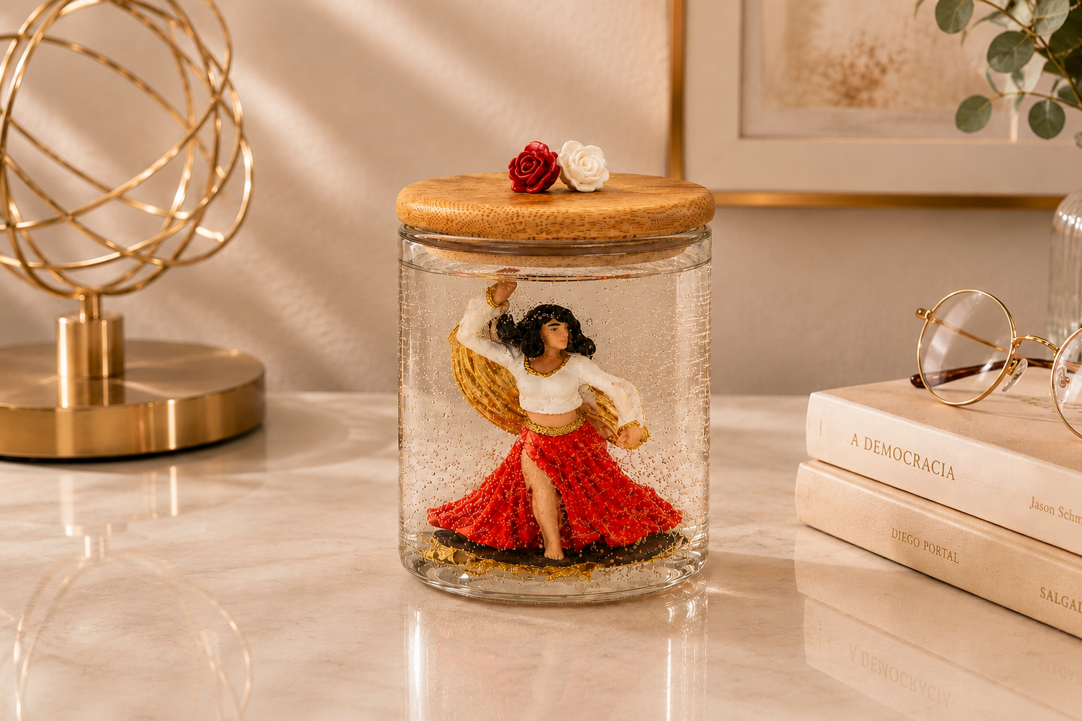 Vela artesanal em gel transparente com figura de Cigana dançando, vestida com saia vermelha e blusa branca, posicionada no interior de um recipiente de vidro com tampa de madeira decorada por duas rosas. A composição está sobre uma mesa clara com elementos sofisticados ao redor, transmitindo elegância, prosperidade e charme.
