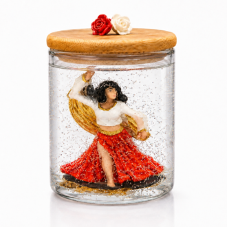Vela artesanal em gel transparente com escultura de Cigana dançando, vestida com saia vermelha e blusa branca com detalhes dourados. A peça está acondicionada em um elegante recipiente de vidro com tampa de madeira decorada por duas rosas, uma vermelha e uma branca, destacando a delicadeza dos detalhes e a transparência do gel.