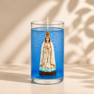 Vela em gel azul transparente com microbolhas decorativas em recipiente cilíndrico de vidro. No interior está uma imagem de Nossa Senhora de Fátima com coroa dourada e mãos unidas em oração. A composição apresenta fundo claro com iluminação suave e sombras naturais de folhas, transmitindo serenidade, fé e elegância.