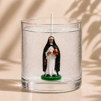 Vela em Gel Santa Edwiges artesanal em recipiente de vidro transparente, com imagem de Santa Edwiges no interior, apresentada sobre fundo bege suave com iluminação natural e sombras delicadas de folhas.