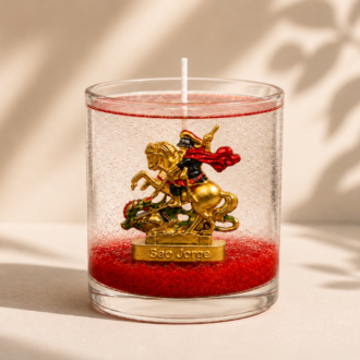 Vela em Gel São Jorge artesanal em copo de vidro transparente, com parafina em gel cristalina e base vermelha decorativa. A peça apresenta a imagem de São Jorge montado em seu cavalo enfrentando o dragão, posicionada em um cenário minimalista com fundo bege claro, sombras suaves de folhagens e iluminação natural que destaca os detalhes da composição.
