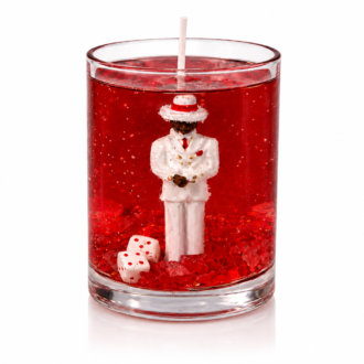 Vela em gel vermelho transparente com escultura de Zé Pilintra vestindo terno branco, gravata vermelha e chapéu tradicional. A composição inclui cristais vermelhos e dados decorativos na base do recipiente de vidro, destacando o simbolismo, a elegância e a personalidade da peça.