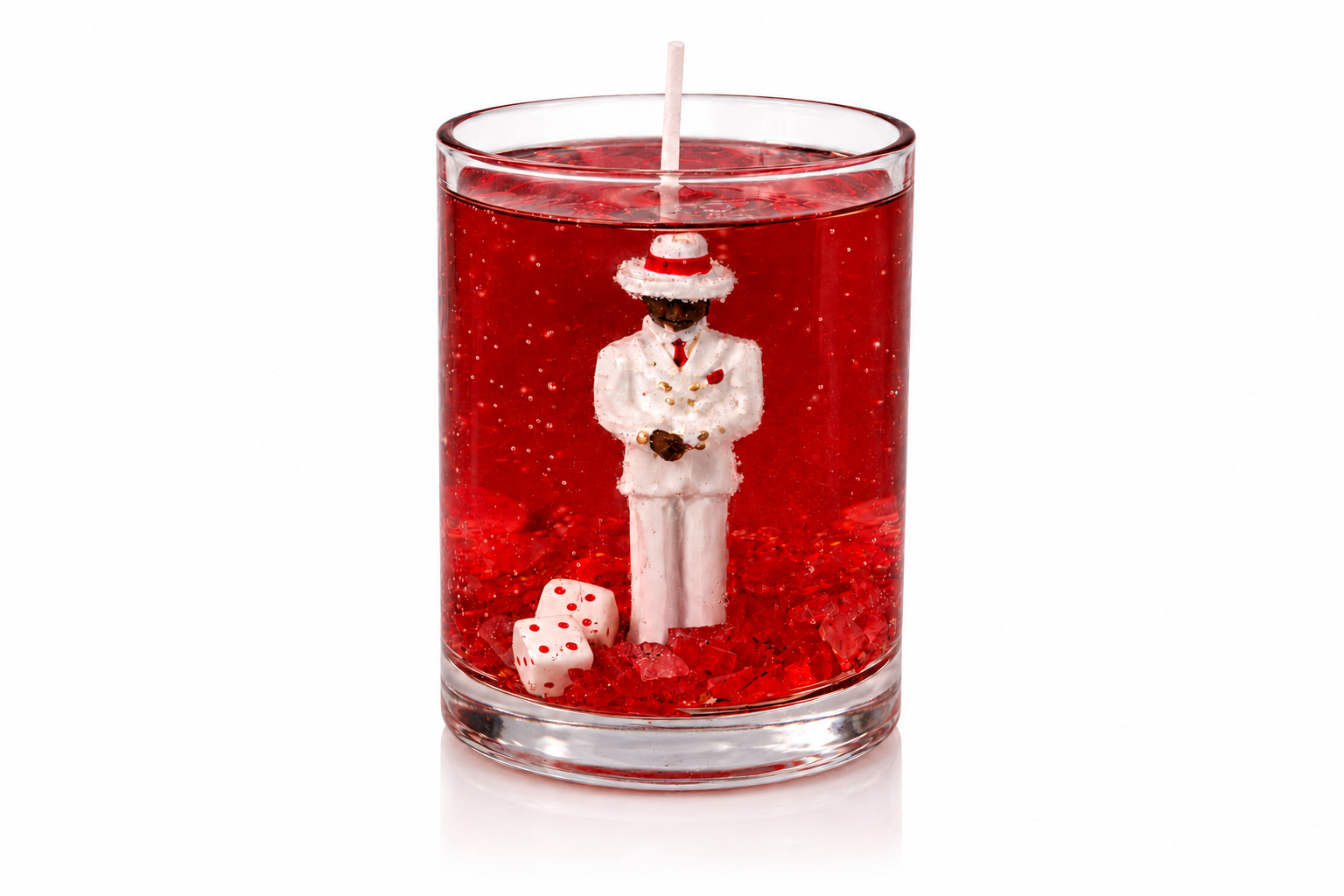Vela em gel vermelho transparente com escultura de Zé Pilintra vestindo terno branco, gravata vermelha e chapéu tradicional. A composição inclui cristais vermelhos e dados decorativos na base do recipiente de vidro, destacando o simbolismo, a elegância e a personalidade da peça.