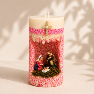 Vela em Gruta Sagrada Família artesanal decorada em tons de rosa e branco, com nicho central contendo as imagens de Maria, José e o Menino Jesus. A peça possui acabamento texturizado com pequenas esferas decorativas, detalhe de cruz dourada na parte frontal e dois pavios na parte superior.