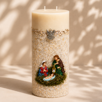 Vela Gruta da Sagrada Família artesanal em formato cilíndrico, decorada com delicados pedriscos claros, detalhes dourados e uma representação da Sagrada Família com Maria, José e o Menino Jesus. A peça está posicionada em um cenário minimalista com fundo bege suave e sombras naturais de folhagens, transmitindo serenidade, fé e elegância.