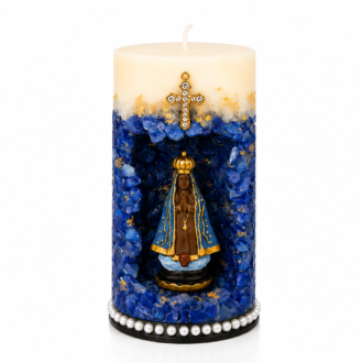 Vela Gruta de Nossa Senhora Aparecida artesanal em tons de azul royal, branco e dourado, com imagem de Nossa Senhora Aparecida posicionada em nicho central decorativo. A peça possui acabamento com cristais azuis, detalhes dourados aplicados manualmente, cruz ornamentada na parte superior e base decorada com pérolas. A fotografia apresenta fundo branco suave, destacando todos os detalhes da vela de forma elegante e profissional.