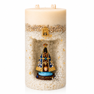 Vela Gruta de Nossa Senhora Aparecida artesanal em formato cilíndrico, com acabamento em tons marfim e textura composta por pequenos cristais decorativos. A peça possui um nicho central com a imagem de Nossa Senhora Aparecida em azul, dourado e preto, acompanhada por delicados detalhes dourados e um pequeno terço decorativo. A vela está apresentada sobre fundo branco em estilo catálogo profissional.