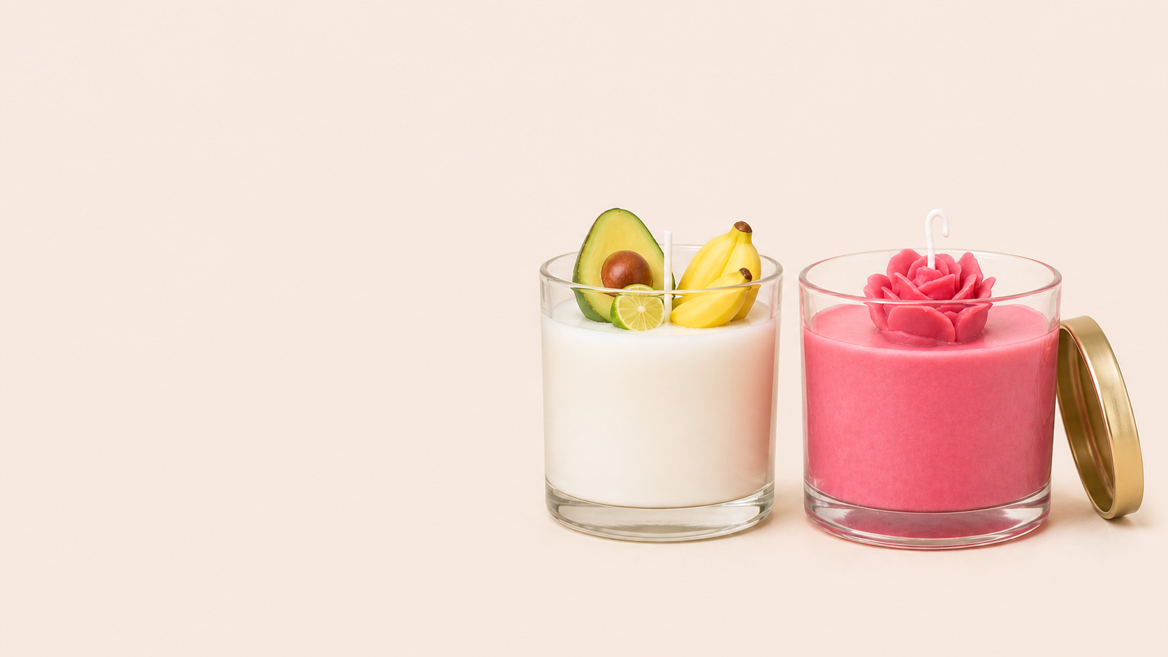 Duas velas decorativas em recipientes de vidro, uma branca com elementos frutados e outra rosa com formato de flor.