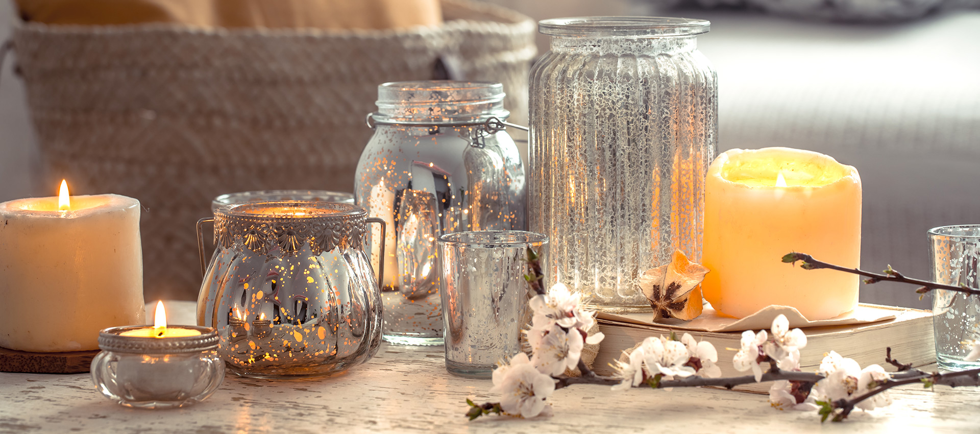 Arranjo decorativo com velas acesas, lanternas e recipientes de vidro refletivos sobre mesa de madeira, acompanhado por flores delicadas em ambiente aconchegante.
